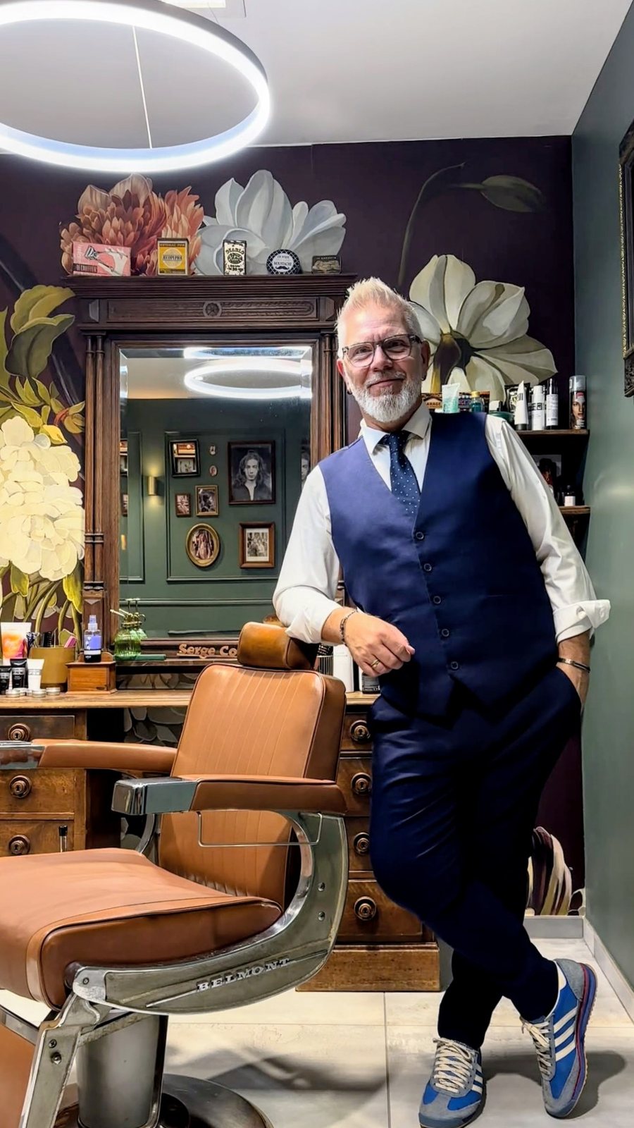 Serge dans son salon à Marchaux, appuyé sur le fauteuil barbier